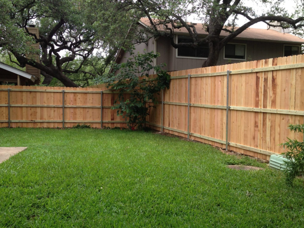 A black metal security fence enclosing a residential backyard with manicured mulch beds and small trees.