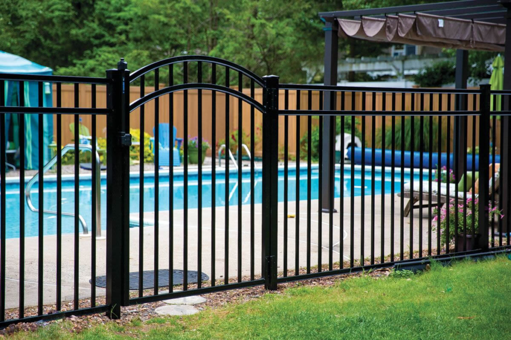 Black aluminum pool safety fence with an arched gate in a backyard setting.