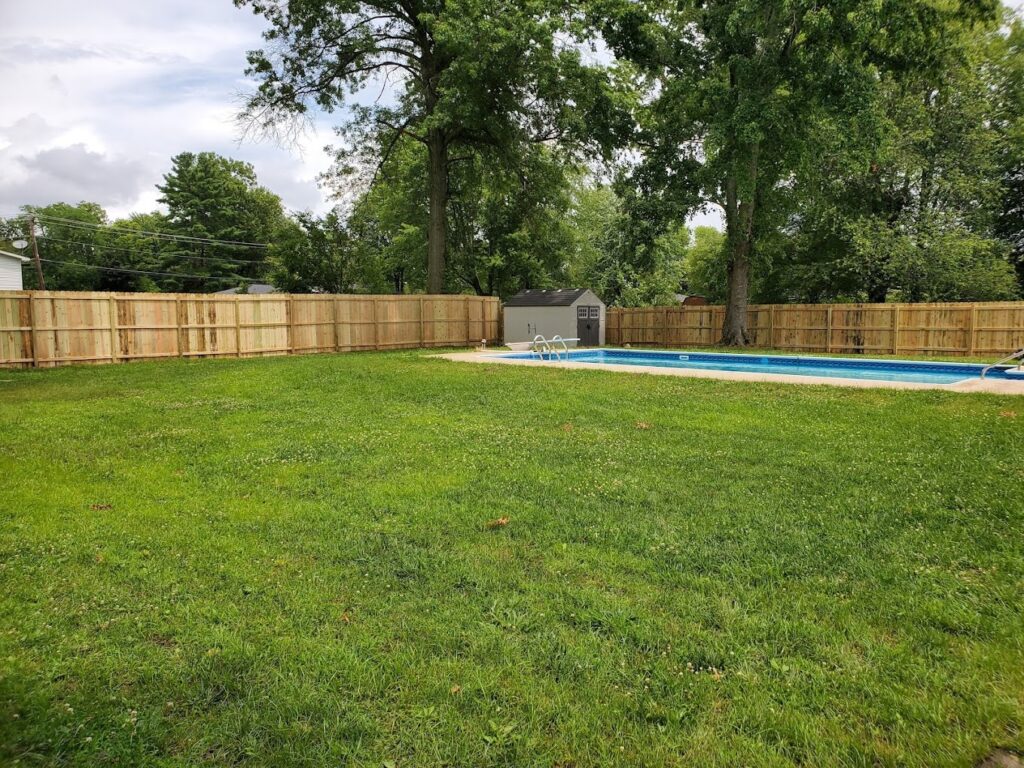 Backyard with a long swimming pool surrounded by a wooden privacy fence.