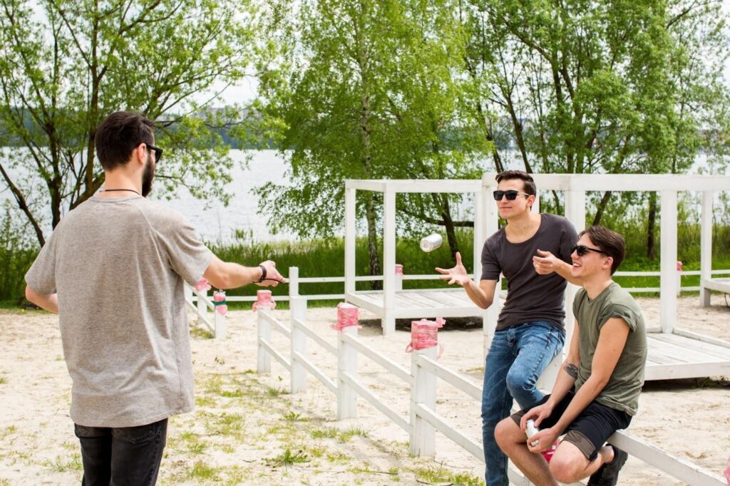 Three friends outdoors by a lake, tossing a can and laughing.